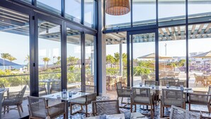 An indoor dining area with large windows, wicker furniture, and a view of the beach. - Planet Hollywood Cancun by Royalton, An Autograph Collection All-Inclusive Resort (Costa Mujeres)