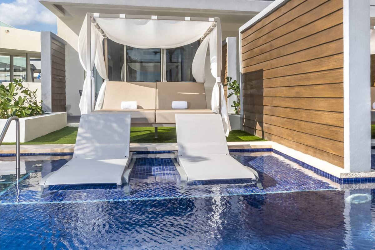 A modern pool area with two lounge chairs and a covered seating area, surrounded by a wooden fence and a glass balustrade.