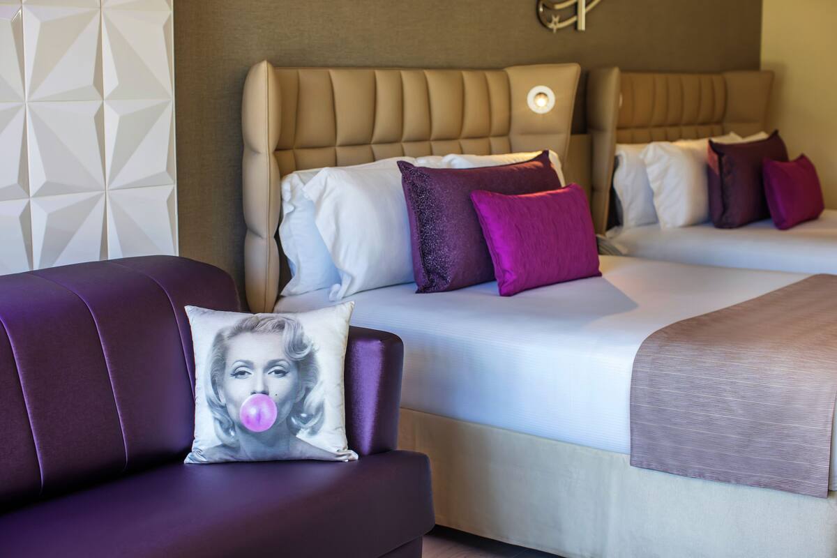 A hotel room with a bed, two pillows, a headboard, and a couch with a pillow.