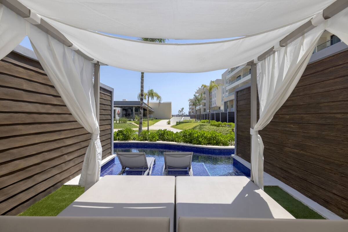 A poolside area with two lounge chairs, a small pool, and a view of a resort building.