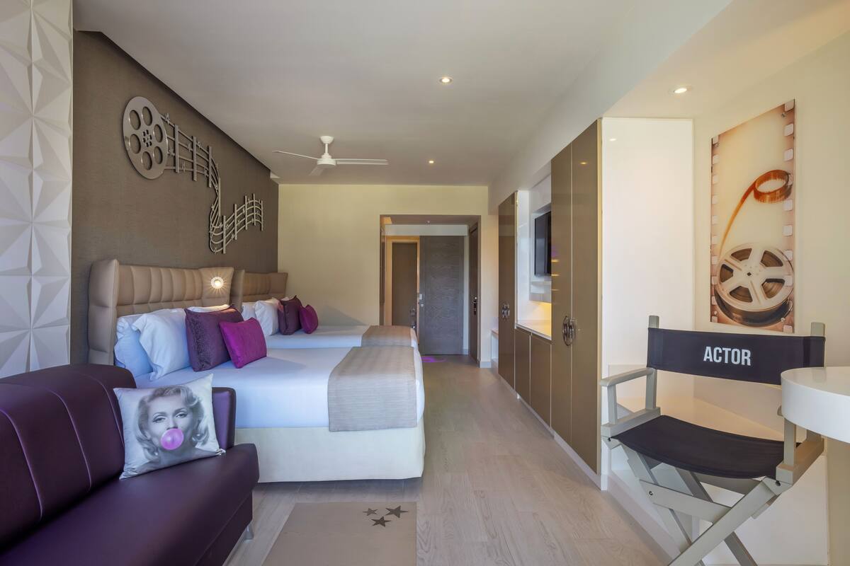 A modern hotel room with a large bed, a sofa, a small table, and a ceiling fan.
