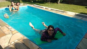 A swimming pool with a stone border and a grassy area in the background. - Casa Aconchegante Lazer e Descanso (Araruama)