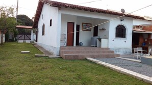 A white house with a tiled roof, a porch with steps, and a small outdoor seating area. - Casa Aconchegante Lazer e Descanso (Araruama)