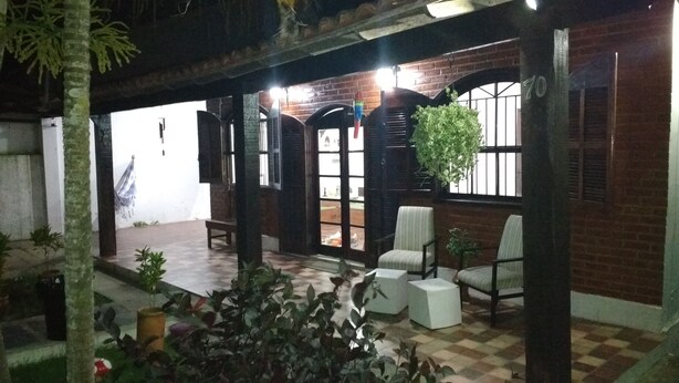 A covered outdoor seating area with brick walls, large windows, and hanging plants. - Casa Aconchegante Lazer e Descanso (Araruama)