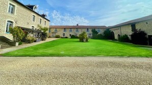 A courtyard with a well-maintained lawn, stone buildings, and a gravel path leading to the entrance. - 3 well equipped gites with swimming pool on the Loire Valley/Vienne border (Prinçay)