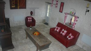 A room with a red sofa, a wooden bench, and a small table with a fruit bowl. There is a white wall with a window and a door. - 3 well equipped gites with swimming pool on the Loire Valley/Vienne border (Prinçay)