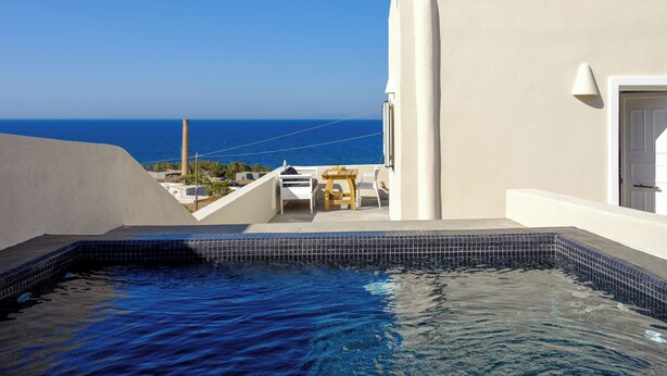 Una piscina con vista sul mare, un edificio bianco e una piccola area salotto all'aperto.