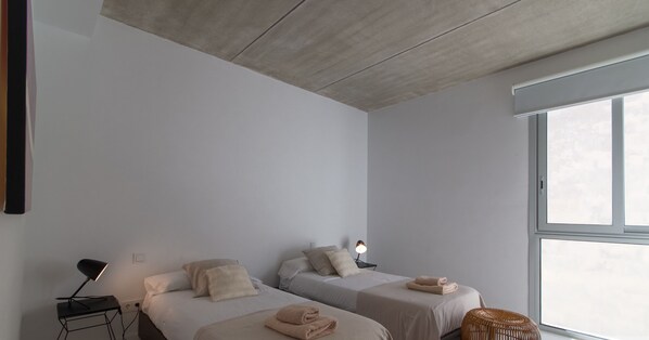 Une chambre moderne avec deux lits, une table de chevet avec une lampe et une grande fenêtre.