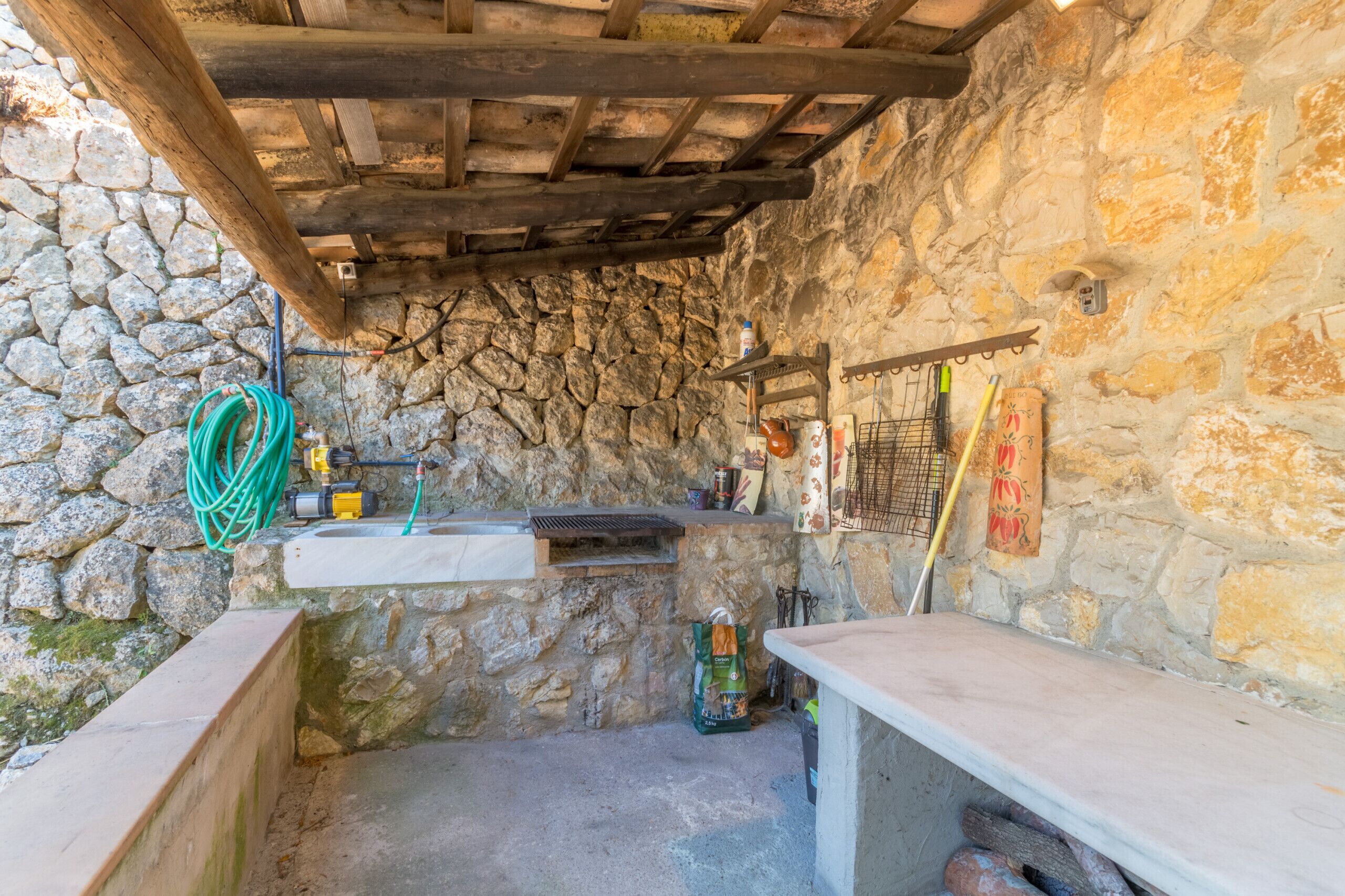 Une cuisine rustique aux murs de pierre, avec un plafond en bois, un évier et divers ustensiles de cuisine.