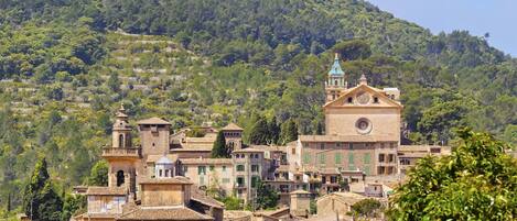 A historic town with terracotta-roofed buildings, a prominent church with a bell tower, and a hillside backdrop.