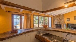 Una cocina con chimenea de piedra, vigas de madera y un amplio ventanal con cortinas.