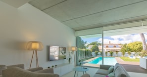 Ein modernes Wohnzimmer mit Blick auf einen Pool, grauem Sofa, einem kleinen runden Tisch und einer Stehlampe.