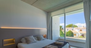 Ein modernes Schlafzimmer mit einem großen Bett, einem Nachttisch und Blick auf die Stadt durch große Fenster.