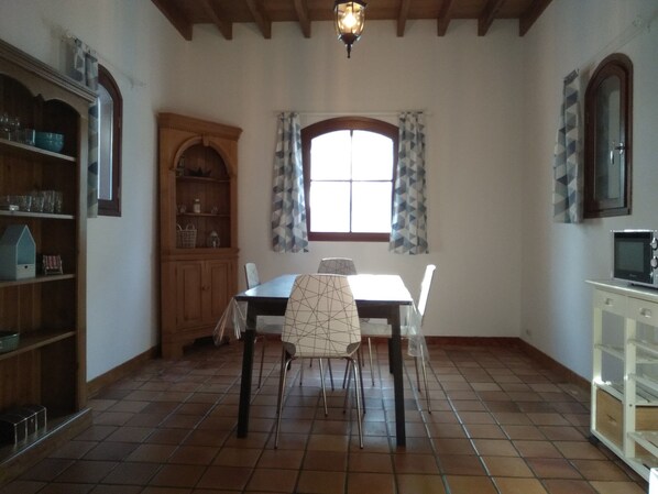 A dining area with a tiled floor, a table with chairs, a wooden cabinet, and a window with curtains.