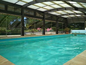A swimming pool with a glass enclosure and a covered roof, surrounded by potted plants and flowers.