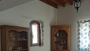 A dining area with a table, chairs, a wooden cabinet with glassware, a window with curtains, and a hanging light fixture. - Near Baie de Somme "good authie" (Colline-Beaumont)