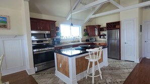 A kitchen with a central island, wooden cabinets, stainless steel appliances, and a white door. - Pierhouse Bed & Breakfast (Kill Devil Hills)
