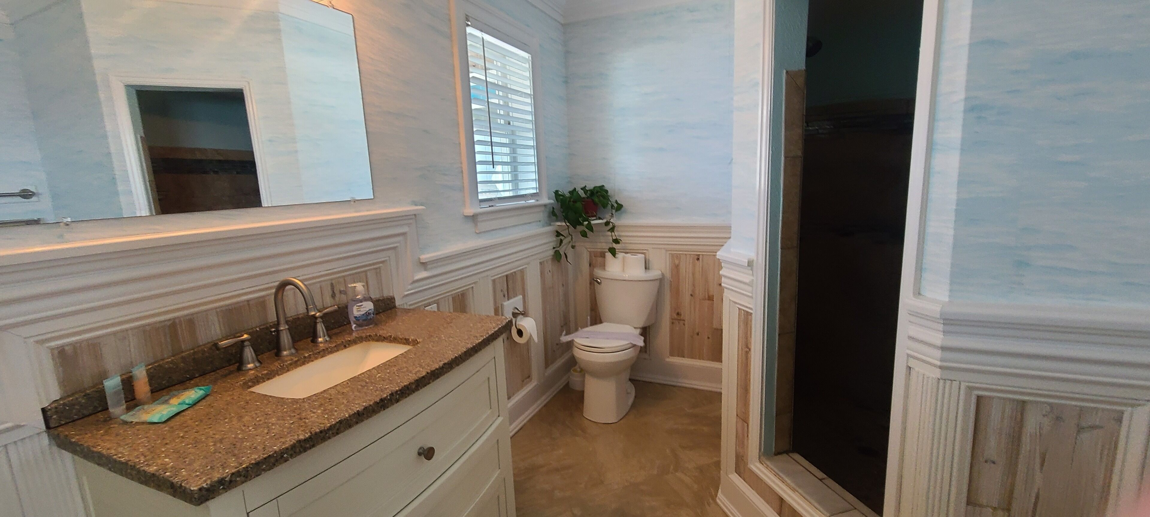 A bathroom with a granite countertop sink, a toilet, and a shower area.