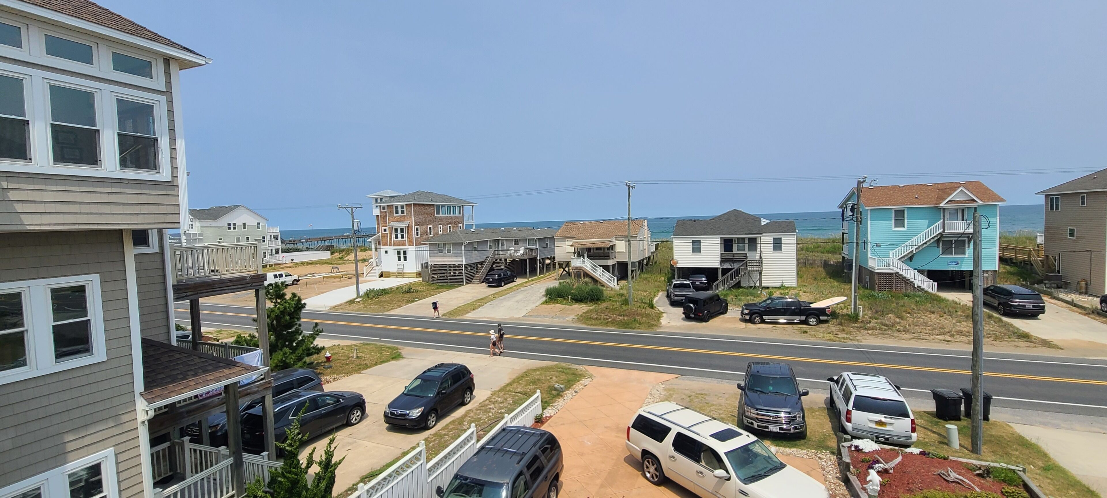 A residential area with houses, a road, and a beach in the background.