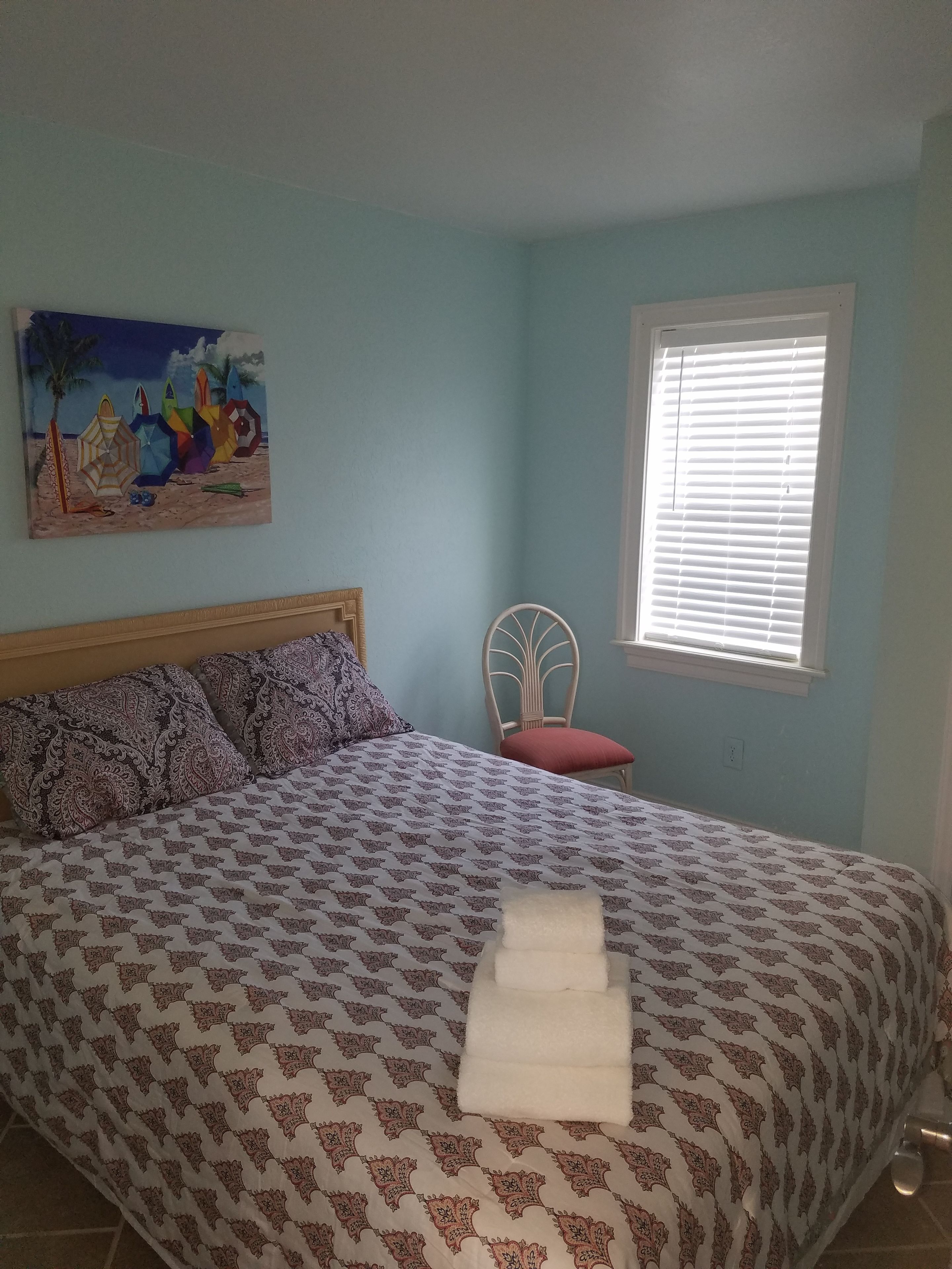 Une chambre à coucher avec un lit, un tableau, une chaise et une fenêtre.