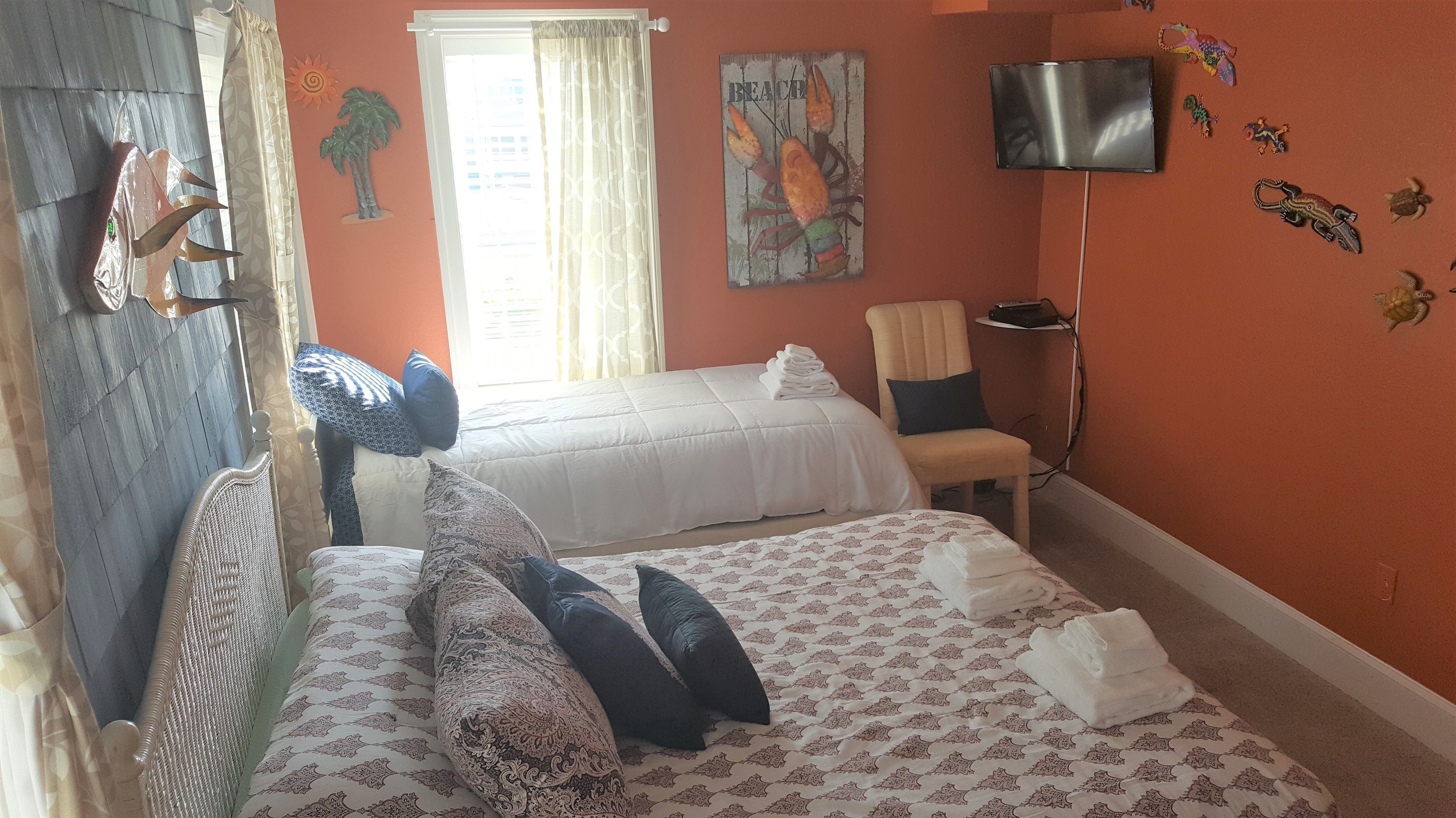A hotel room with two beds, a TV, and a beach-themed wall decoration.
