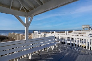 Um deck de madeira com guarda-corpos brancos com vista para uma praia.