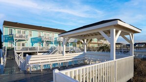 A beachfront hotel with multiple balconies, a wooden deck, and a covered area.