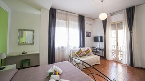 A hotel room with a bed, a desk, a chair, a television, and a balcony with curtains.