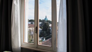 A window with a view of a blue-domed building, curtains, and a tiled roof.