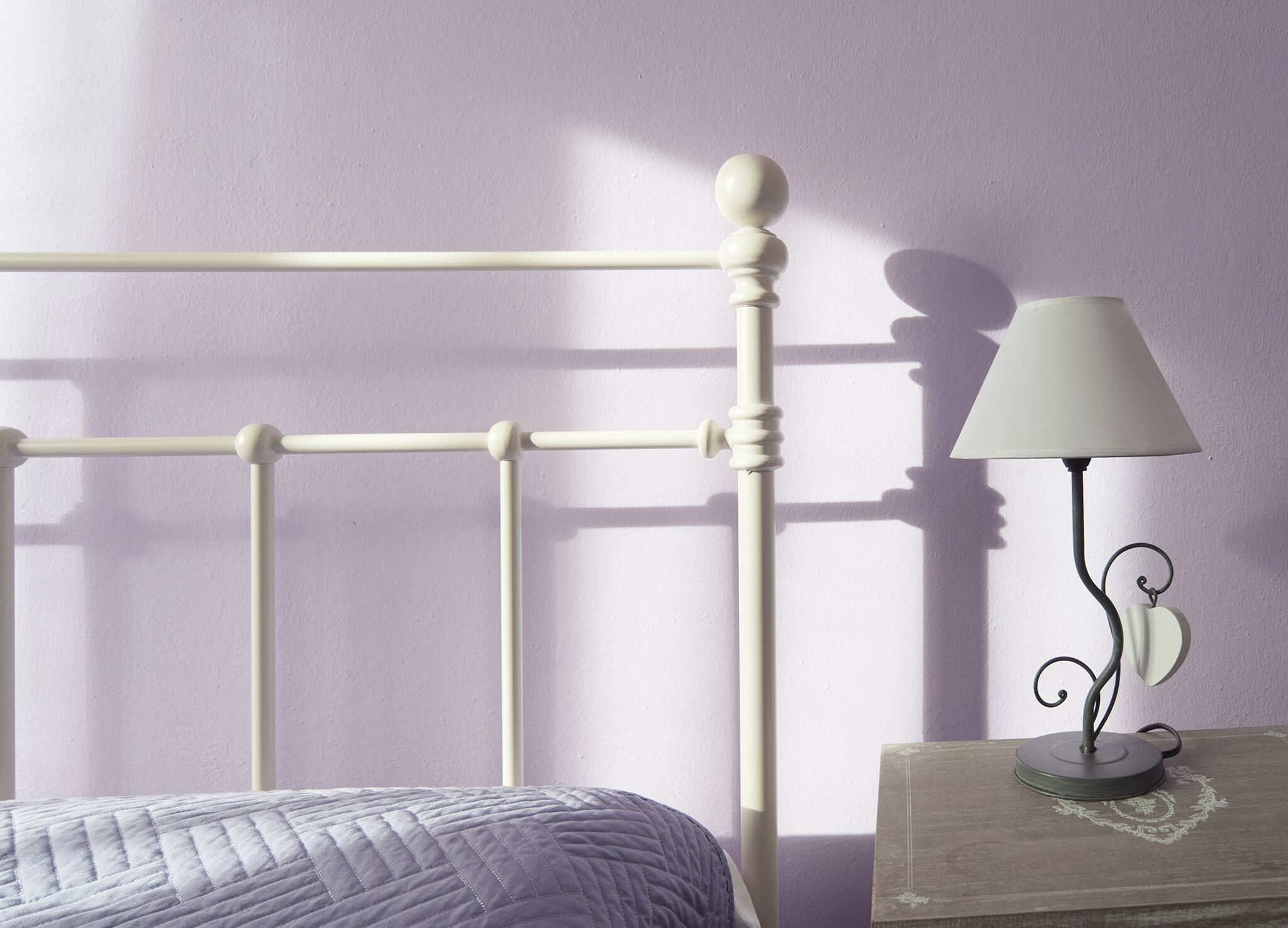 A bed with a white headboard, a bedside table with a lamp, and a wall with a shadow.