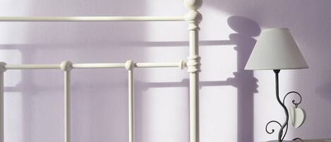 A bed with a white headboard, a bedside table with a lamp, and a wall with a shadow.