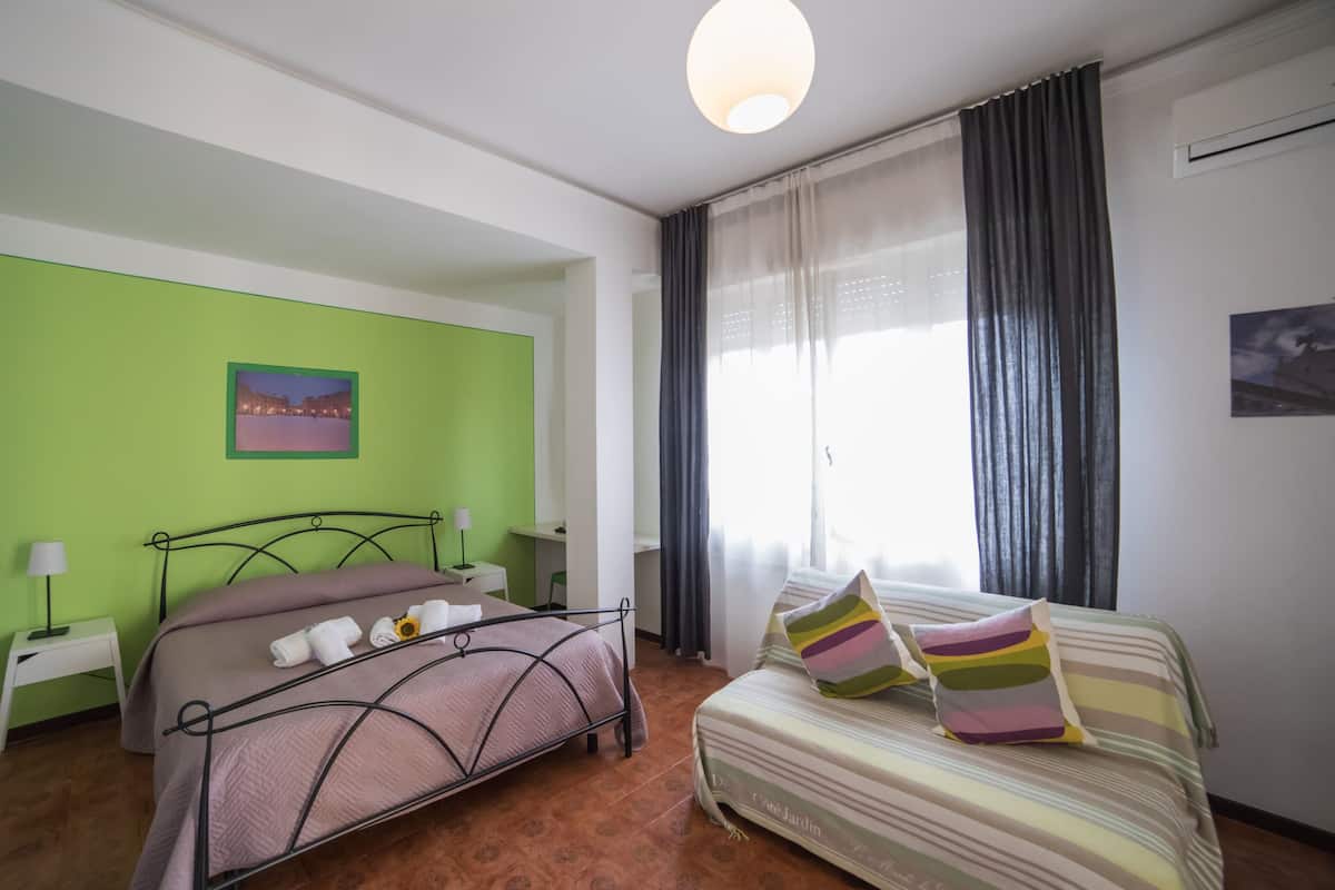 Un dormitorio con dos camas, una pared verde, una ventana con cortinas y una lámpara en el techo.
