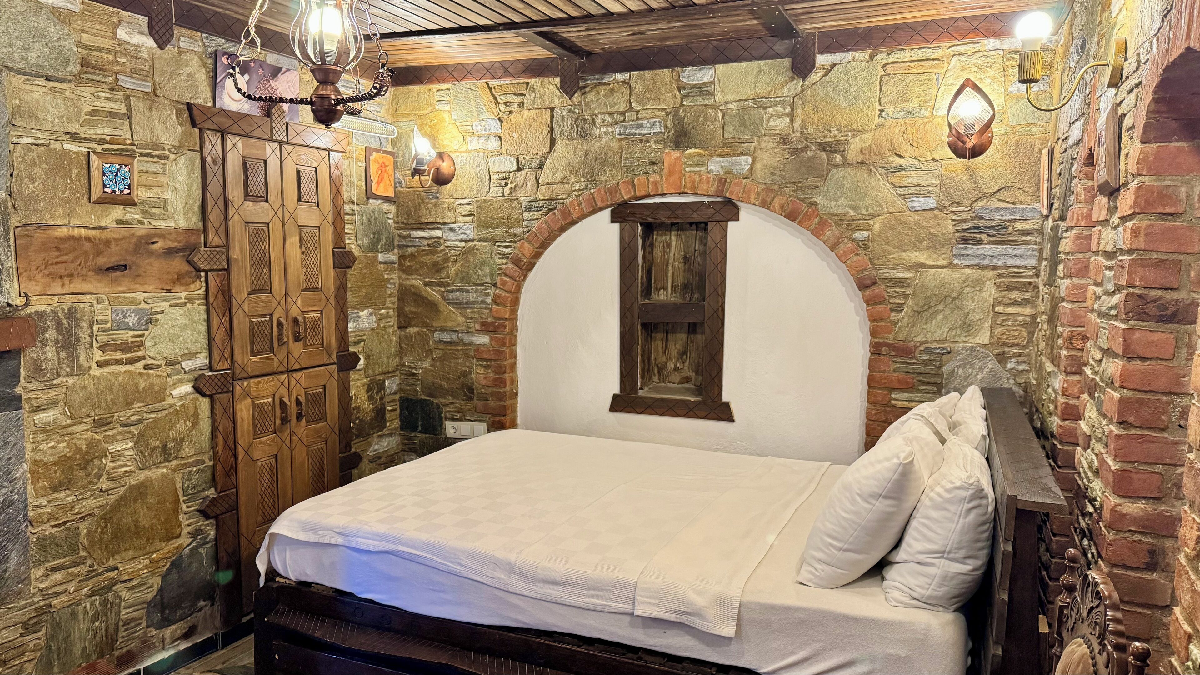 Ein Schlafzimmer mit Steinwand, Holzschrank und Bett mit weißer Bettwäsche.