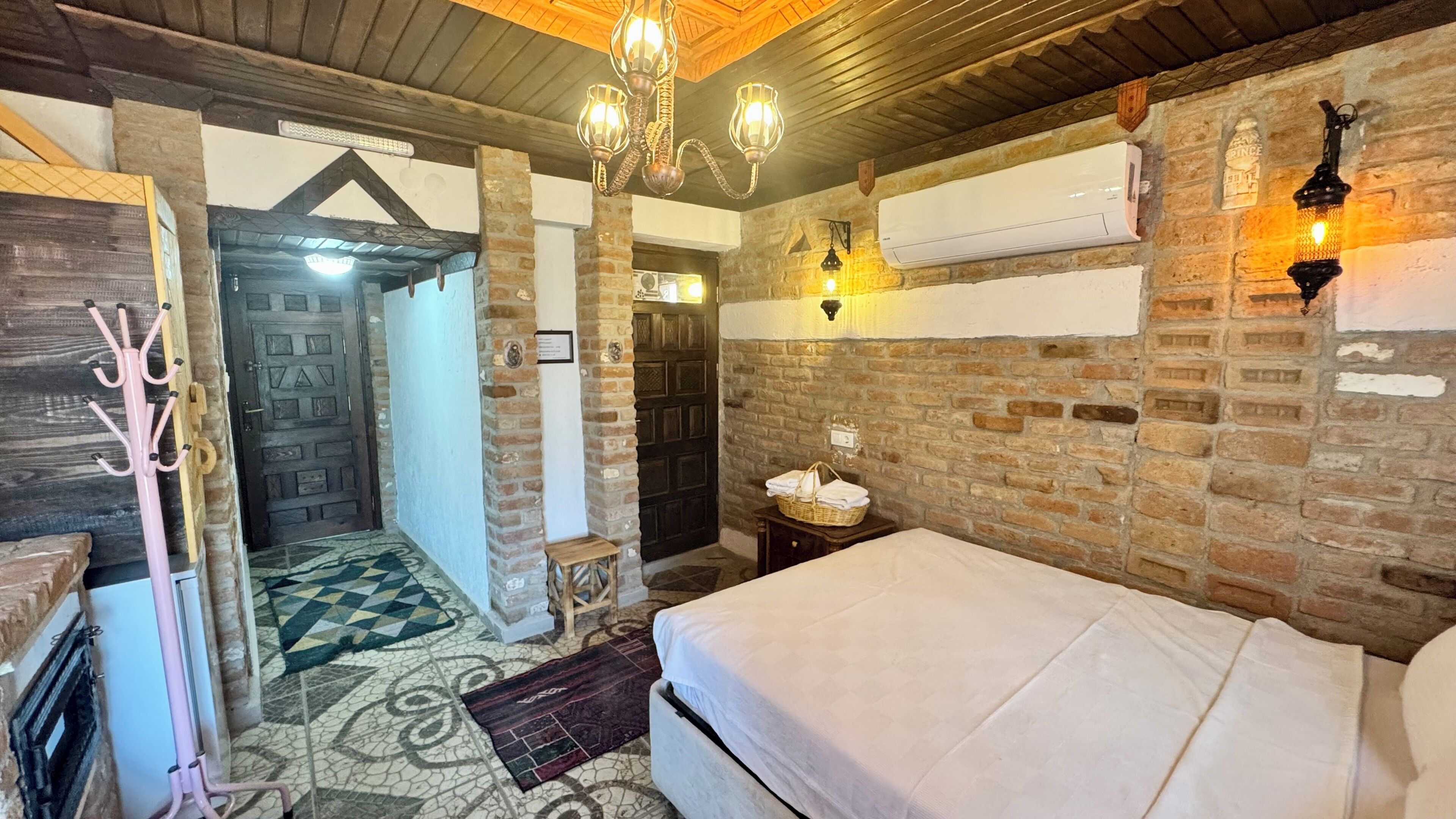 A rustic room with a bed, a coat rack, a door, and a wall-mounted air conditioner.