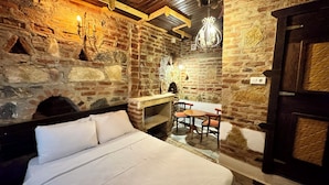 A rustic stone room with a bed, a table, chairs, and a chandelier. - Limaki Konak Sirince (Selçuk)