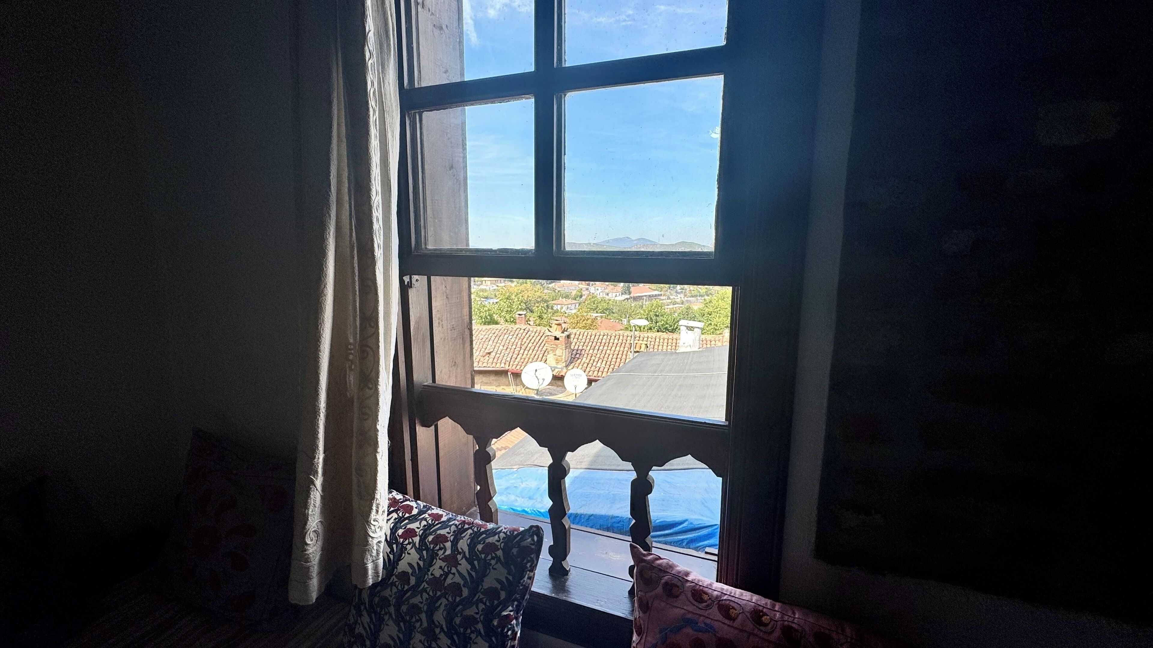 A room with a view through a window with a wooden frame and a balcony.