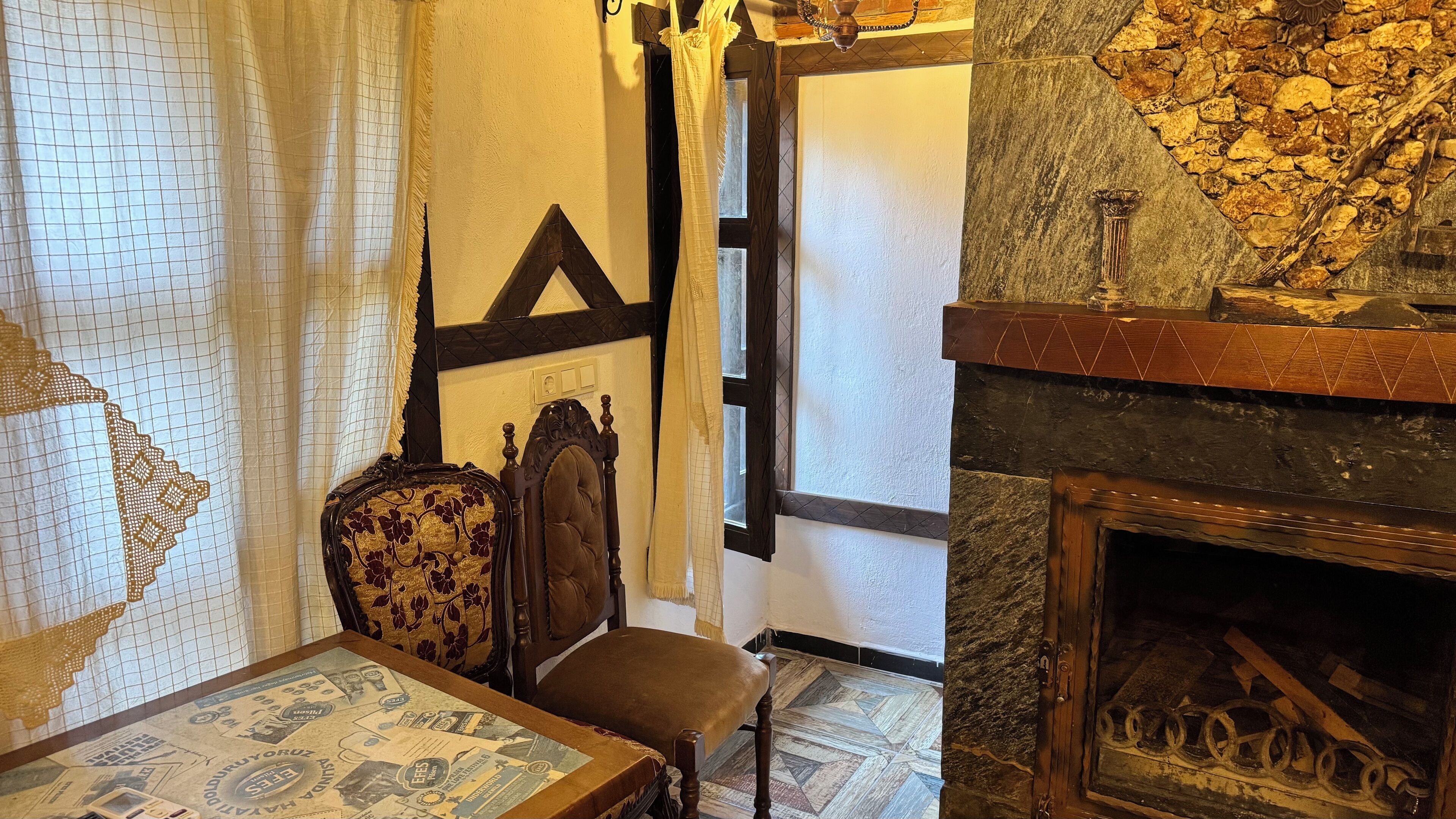 A room with a fireplace, a bed with a patterned bedspread, a wooden chair, and a wall with a geometric design.