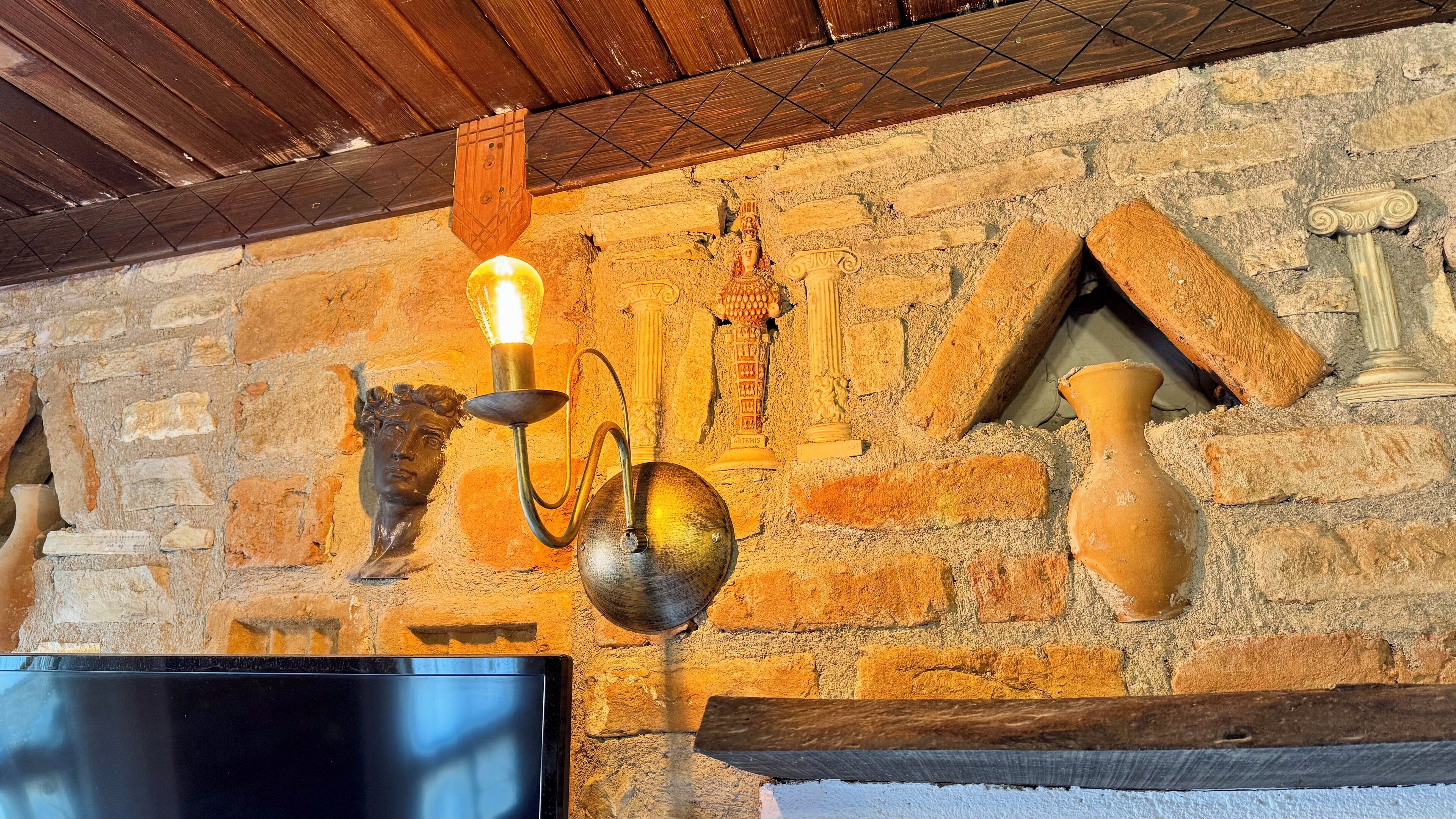 A stone wall with a mounted light fixture, a decorative vase, and a television screen.