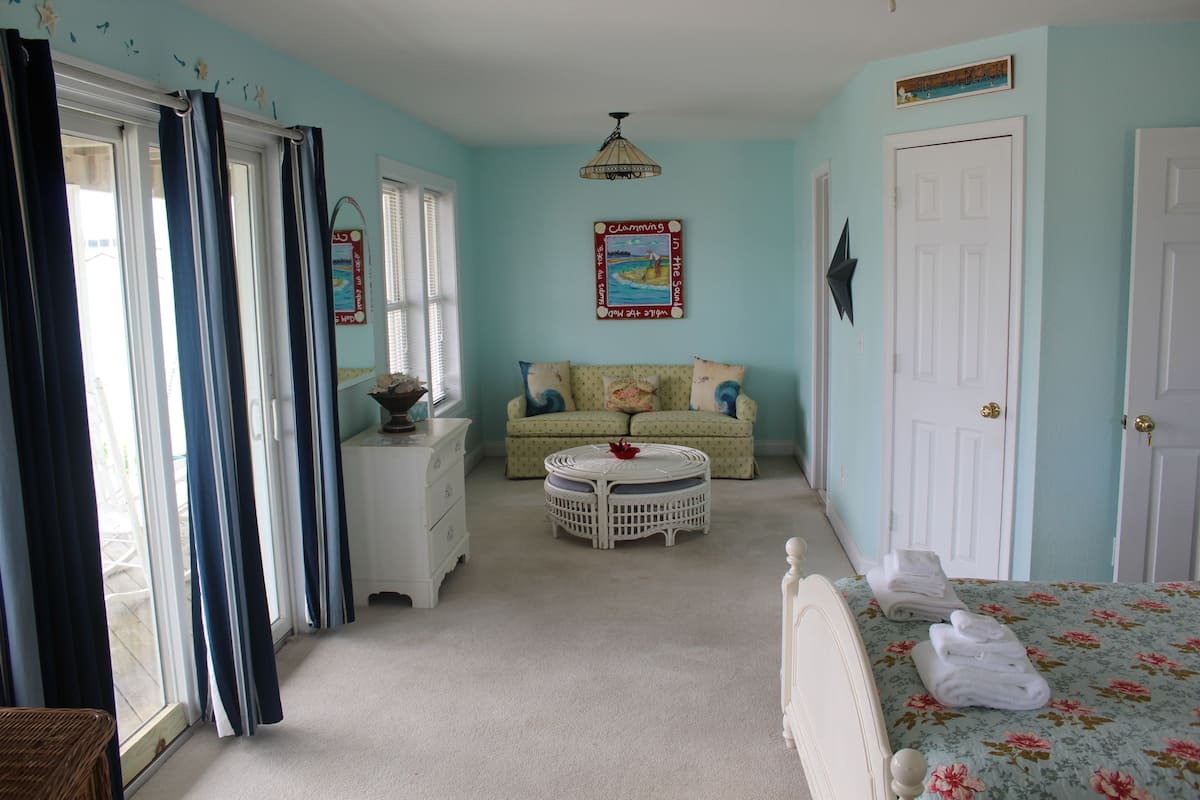 A room with a bed, a round coffee table, a sofa, and a window with curtains.