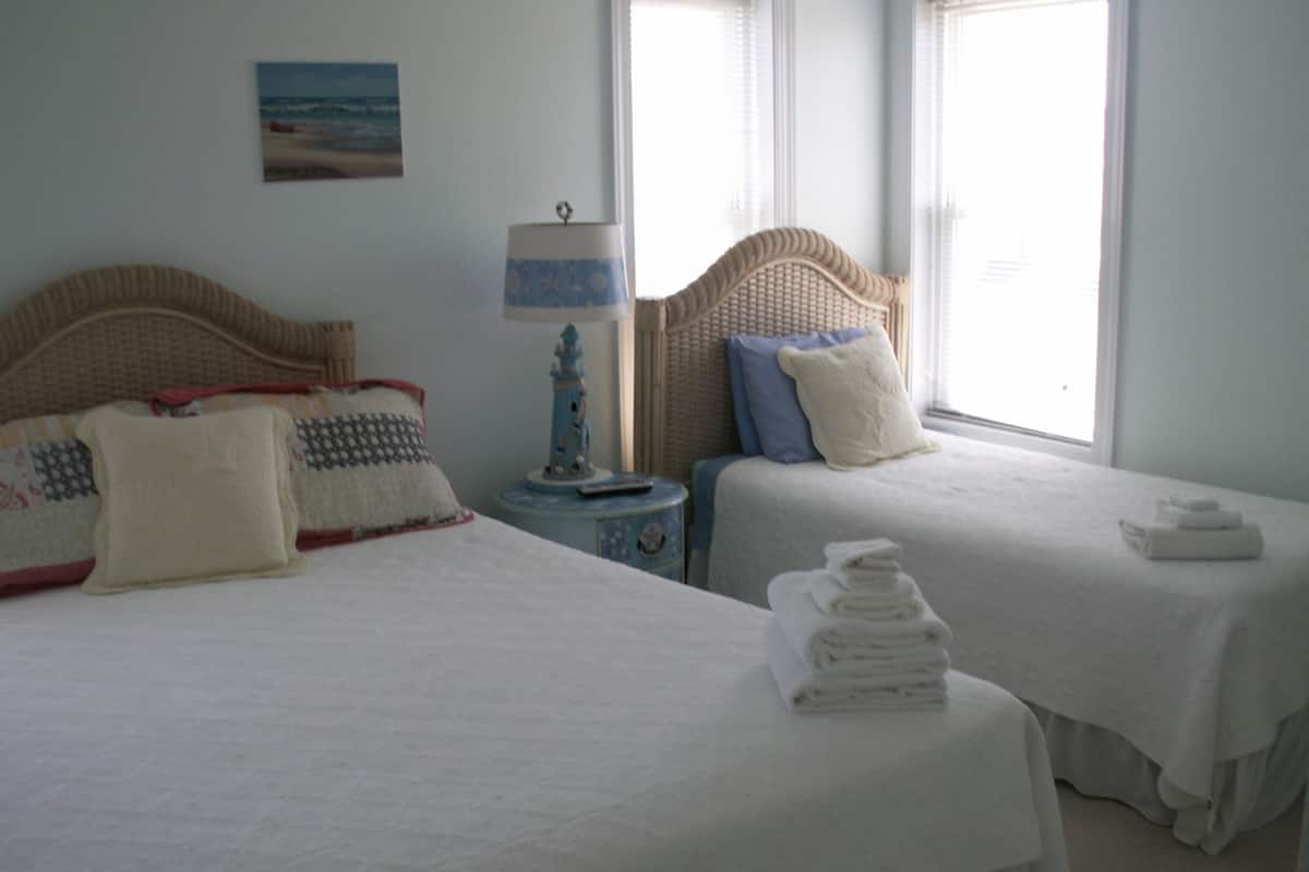 A hotel room with two beds, each with white linens and decorative pillows. There is a small table with a lamp between the beds.
