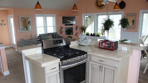 A kitchen with a built-in stove, oven, and countertop. There are cabinets, a sink, and a window with plants. - Sandbar Bed & Breakfast (Nags Head)