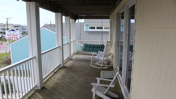 A wooden porch with white railings, a swing chair, and a rocking chair. - Sandbar Bed & Breakfast (Nags Head)