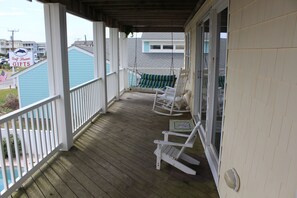 A wooden porch with white railings, a swing chair, and a rocking chair. - Sandbar Bed & Breakfast (Nags Head)