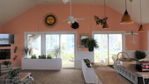 A living room with a ceiling fan, large windows, and a television. - Sandbar Bed & Breakfast (Nags Head)
