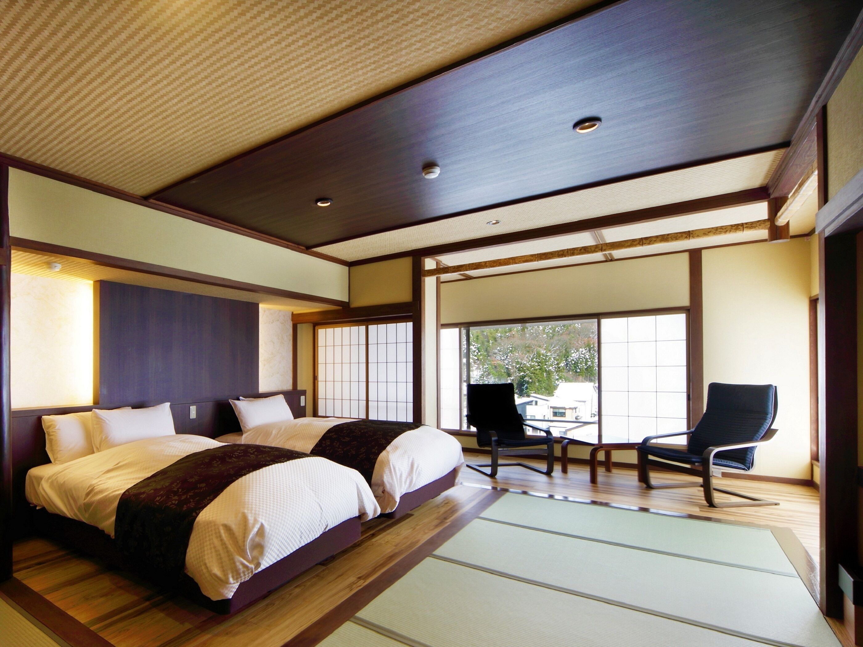A traditional Japanese-style room with tatami flooring, a large bed with white bedding, a desk with a chair, and a sliding shoji screen door.
