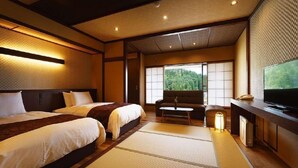 A traditional Japanese-style hotel room with tatami flooring, a sofa, a television, and a view of a forest. - Hotel Hisagoso (Shibata)