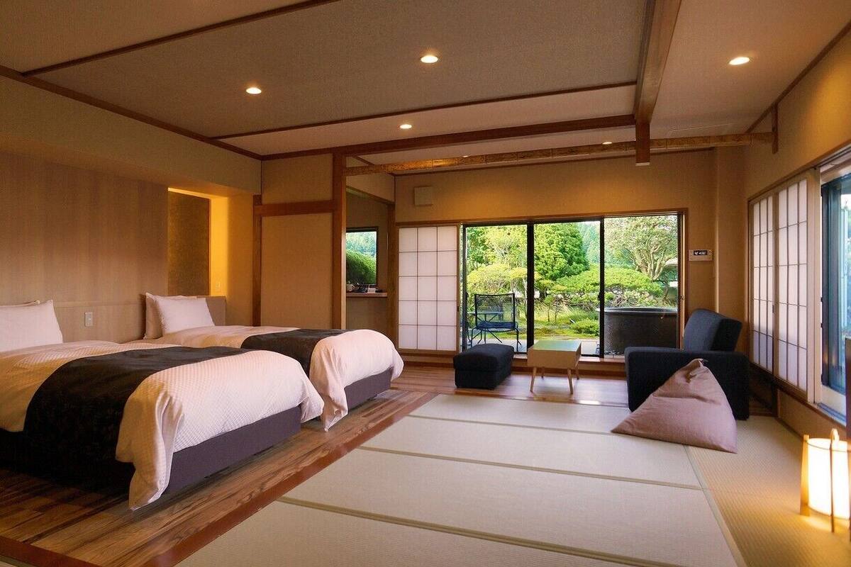 A traditional Japanese-style bedroom with tatami flooring, two beds, a sliding door to a garden, and a view of greenery.