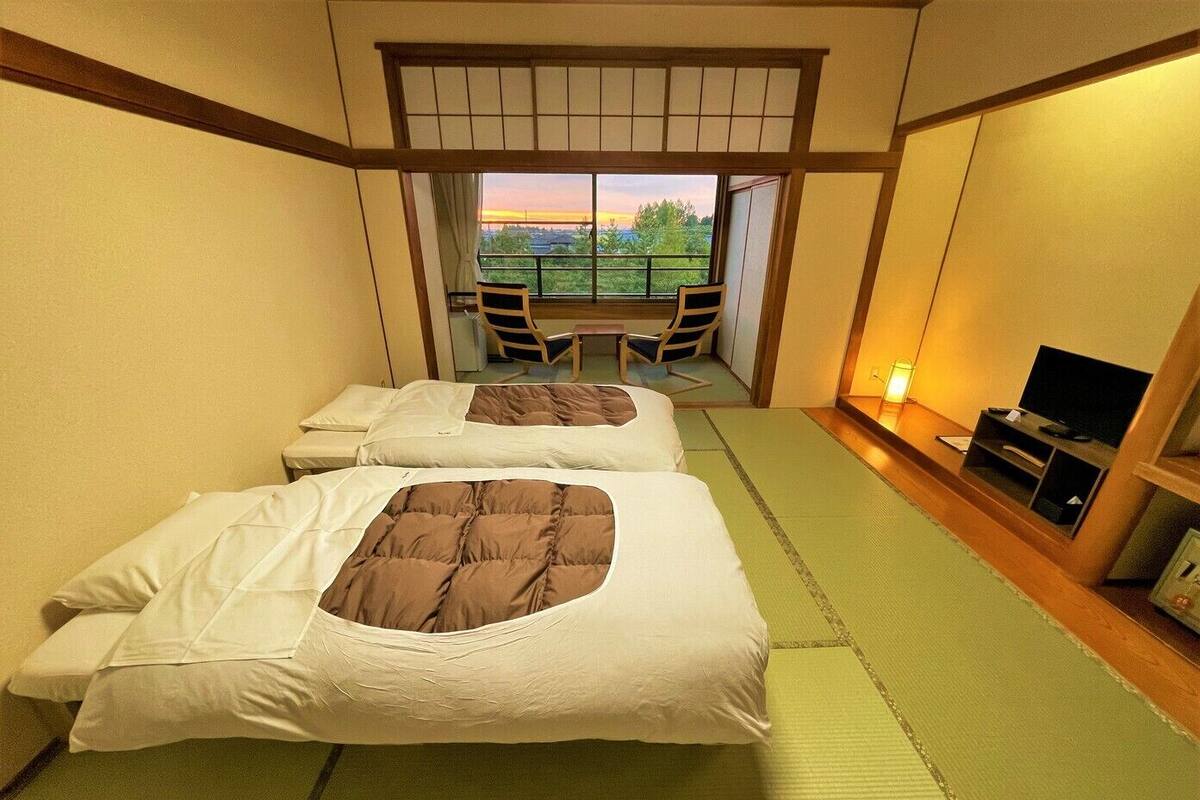 A hotel room with two beds, a TV, and a view of a balcony with chairs.