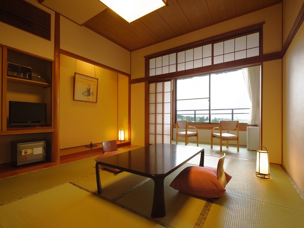 A traditional Japanese room with tatami flooring, a low table, chairs, a television, and a window with a view.