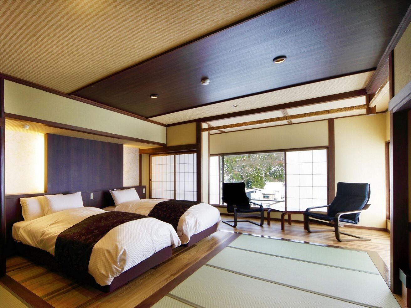 A traditional Japanese-style bedroom with tatami flooring, a large bed, sliding doors, and a view of the outside.